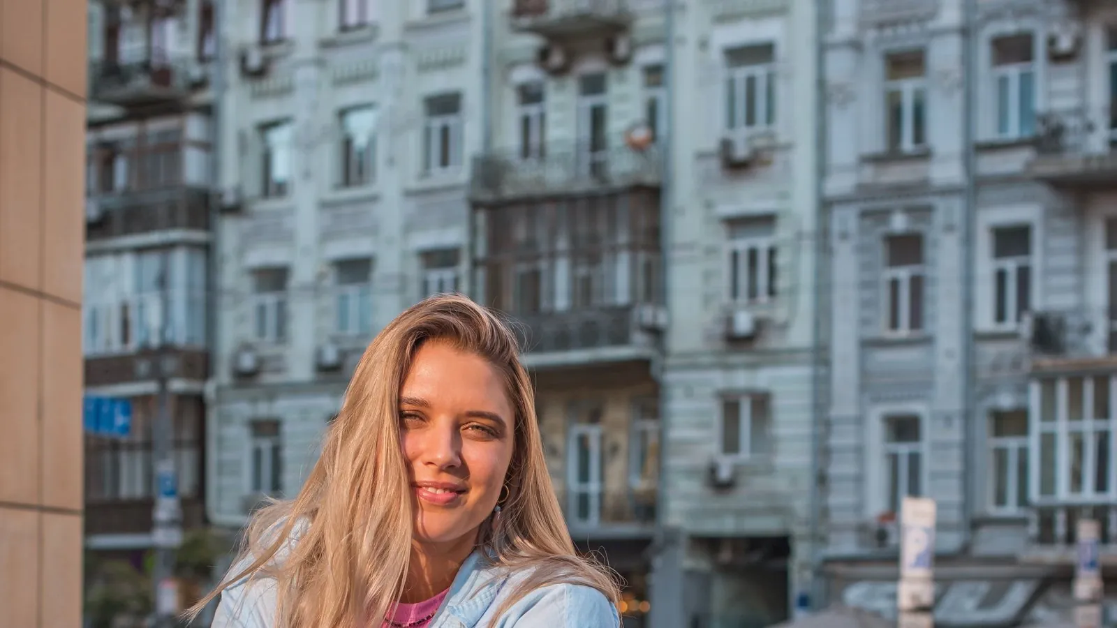 A woman smiling on a city street, holding a coffee